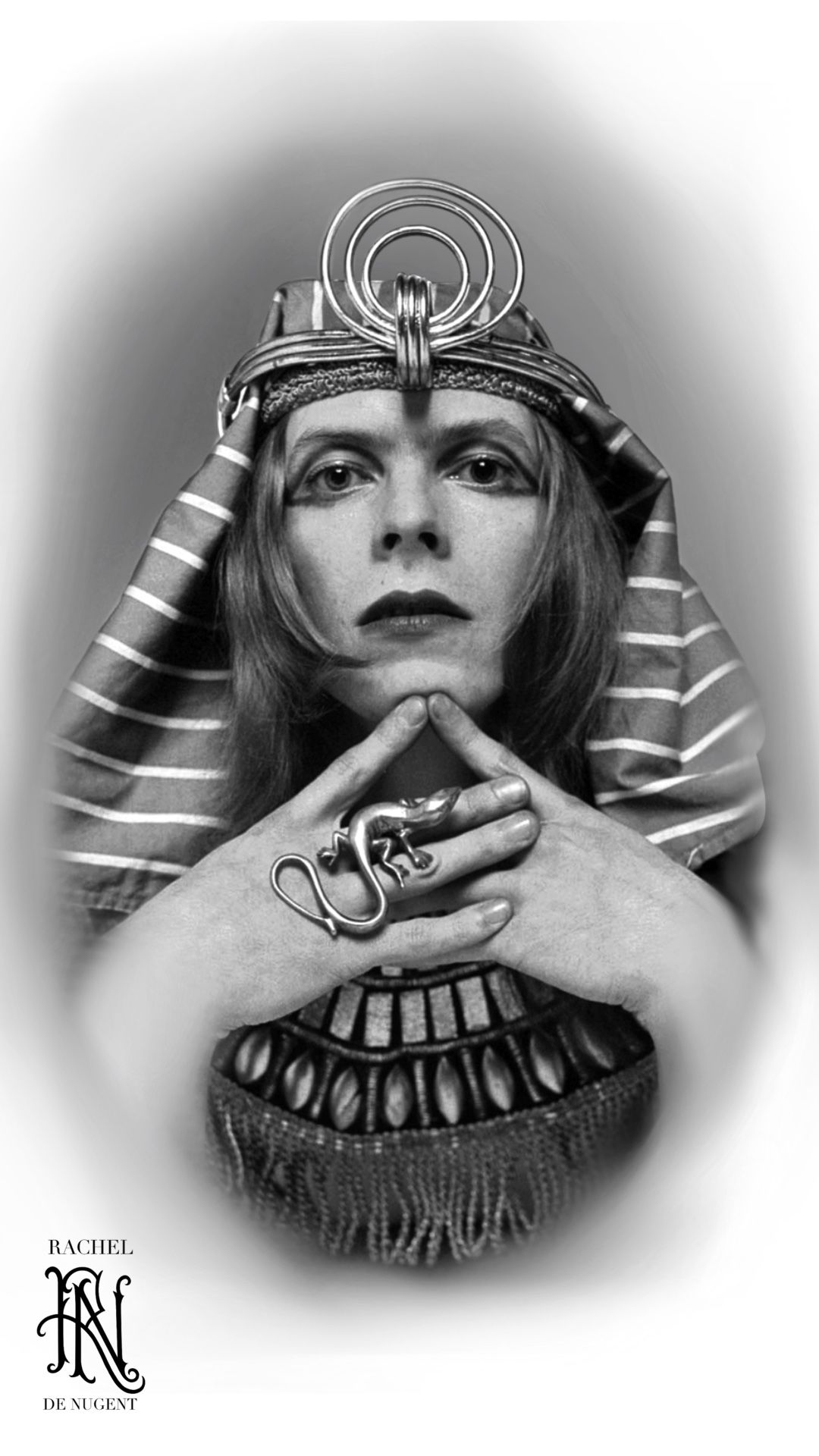 Person in ornate Egyptian-inspired headdress, staring forward with hands clasped under chin.