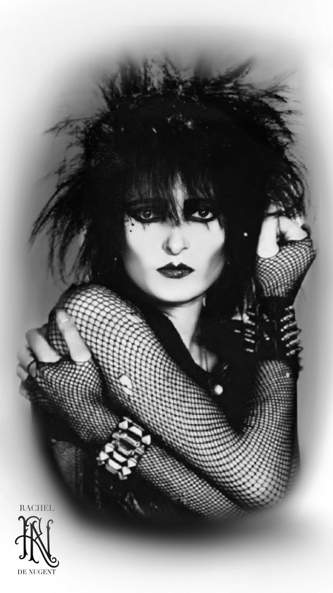 Black-and-white portrait of a person with spiked hair, dark makeup, and fishnet sleeves posing dramatically