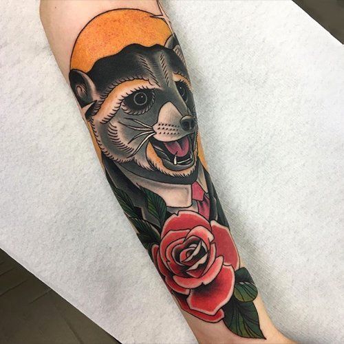 A tattoo of a raccoon and a rose on a person 's forearm.