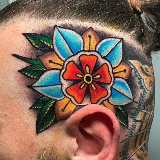 A man has a colorful flower tattoo on his forehead.