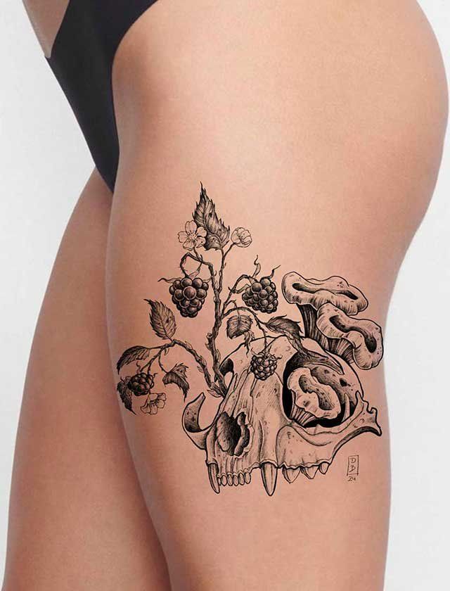 A woman has a tattoo of a skull surrounded by flowers on her thigh.