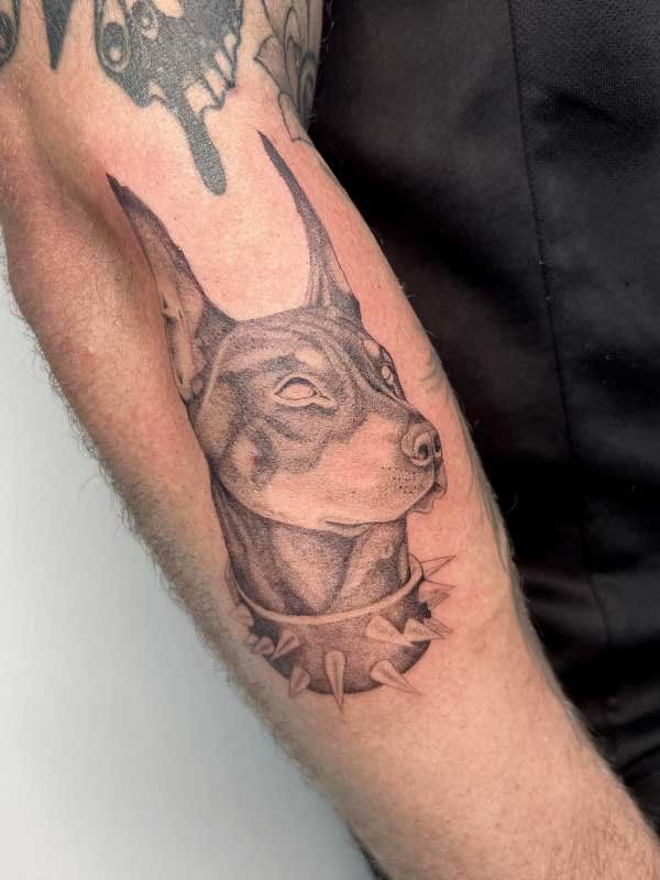 A man has a tattoo of a dog wearing a collar on his arm.