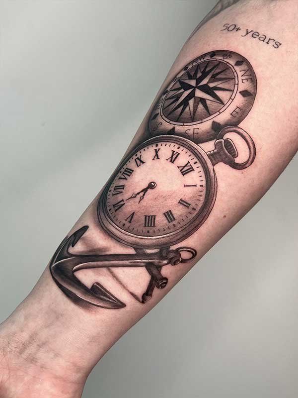 A man has a tattoo of a pocket watch , compass and anchor on his forearm.