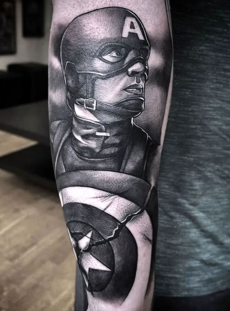 Black-and-gray Captain America tattoo on a person’s upper arm, showing the shield and masked face