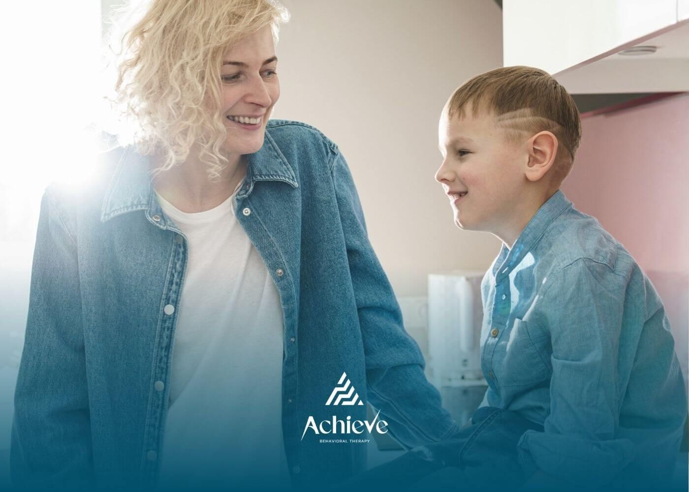 BCBA smiling and talking with a child in a bright kitchen during in-home ABA therapy.