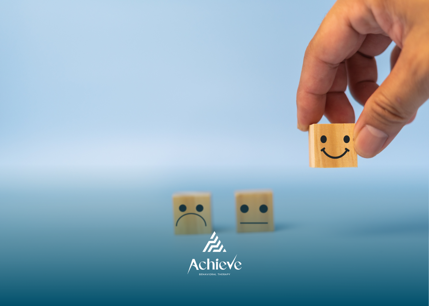 Hand placing a smiling face block. Two blocks show a sad and neutral face against a blue background.