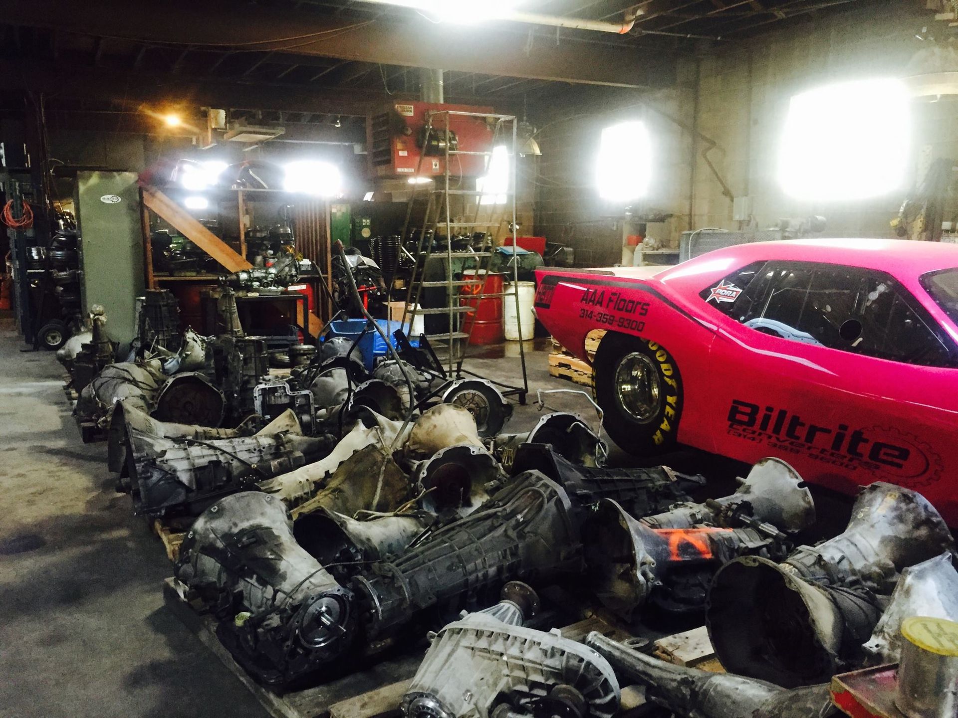 A pink car is parked in a garage next to a pile of parts