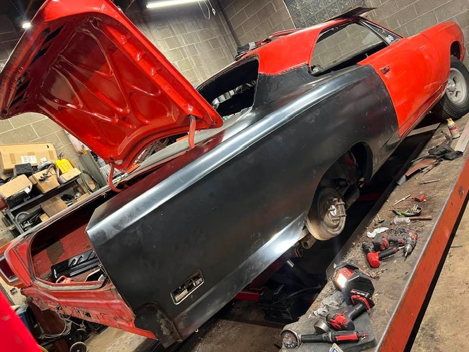 A red car with the hood up is being worked on in a garage.