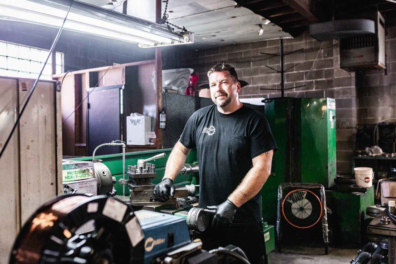 A man is standing in front of a lathe in a garage.