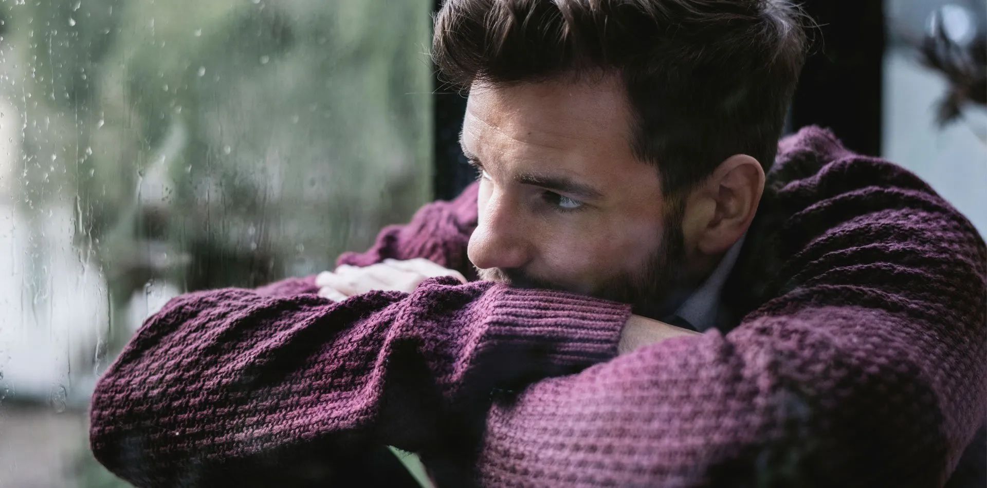 A man in a purple sweater is looking out of a window.