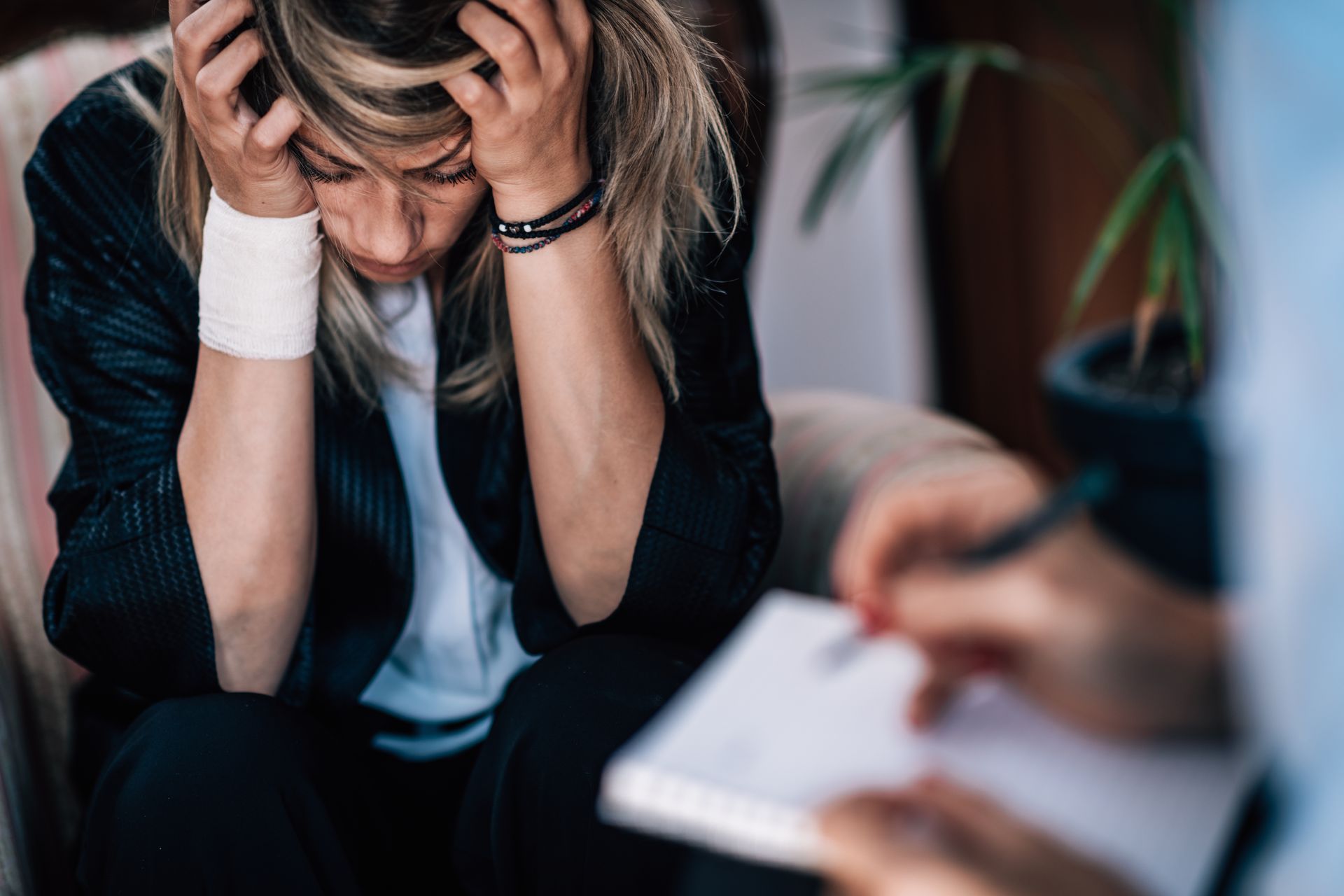 A woman is sitting in a chair with her head in her hands while a person writes on a piece of paper.