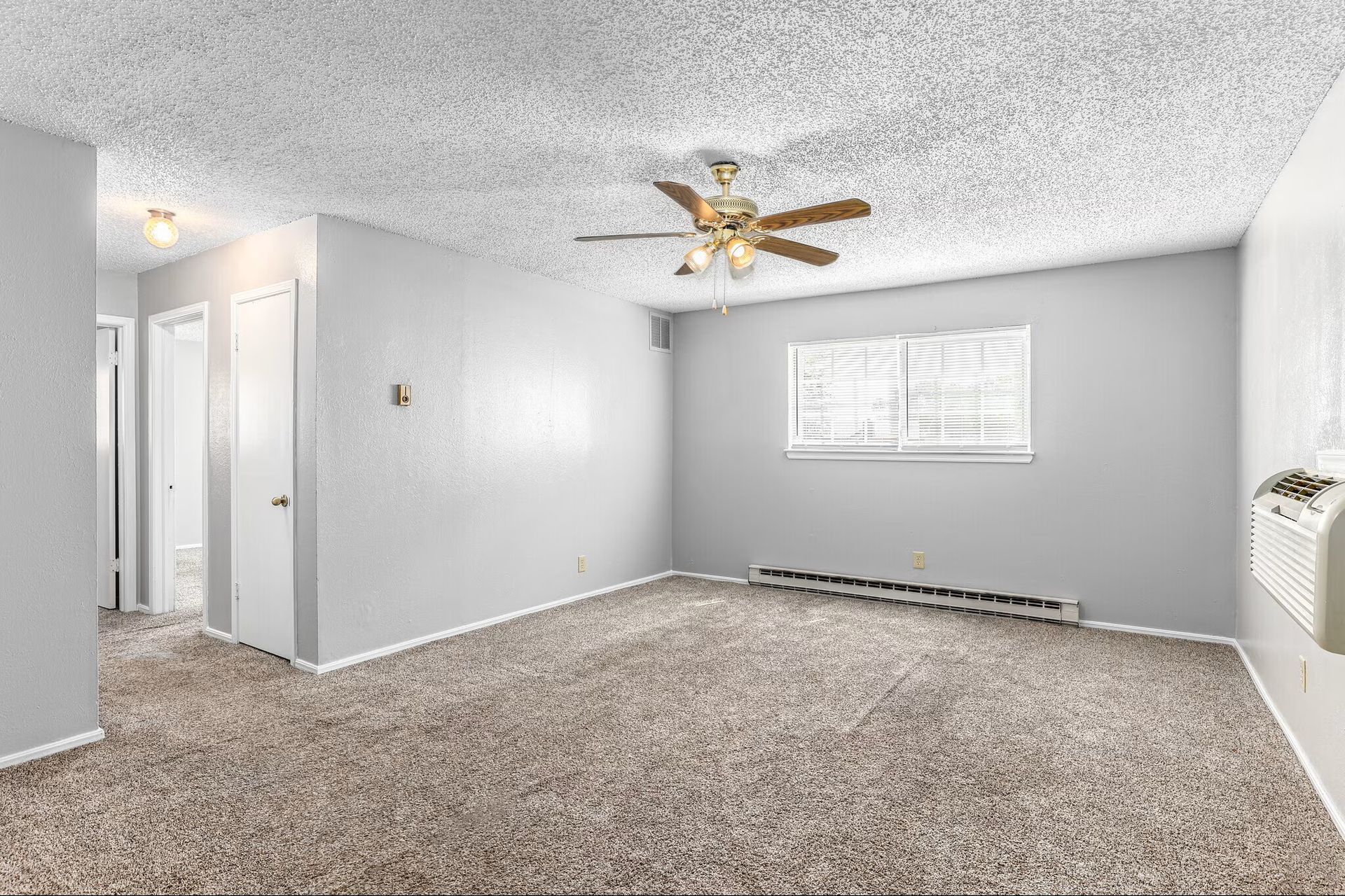 Empty living room with beige carpet, ceiling fan, and small kitchen pass-through.
