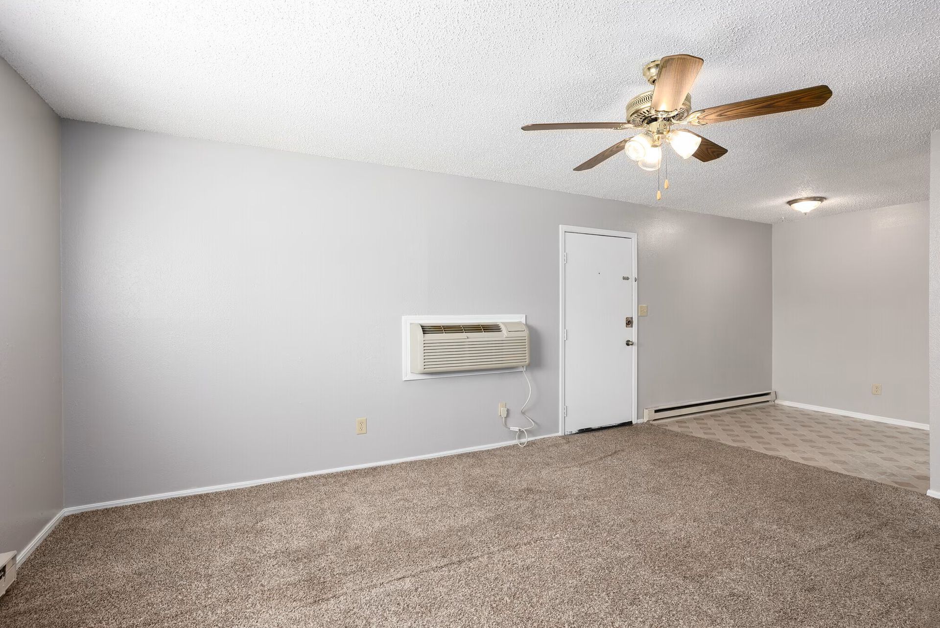 Empty carpeted room with gray walls, ceiling fan, and wall-mounted air conditioner