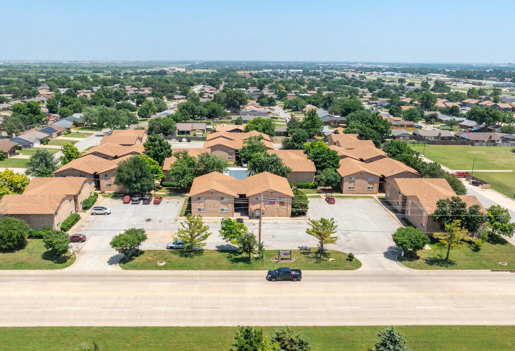 Aerial view of a suburban housing complex with red-tiled roofs, parking lots, and a wide road in front.