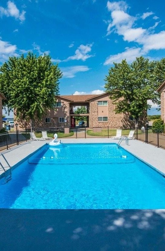 Apartment pool with turquoise umbrellas beside brick buildings on a sunny day