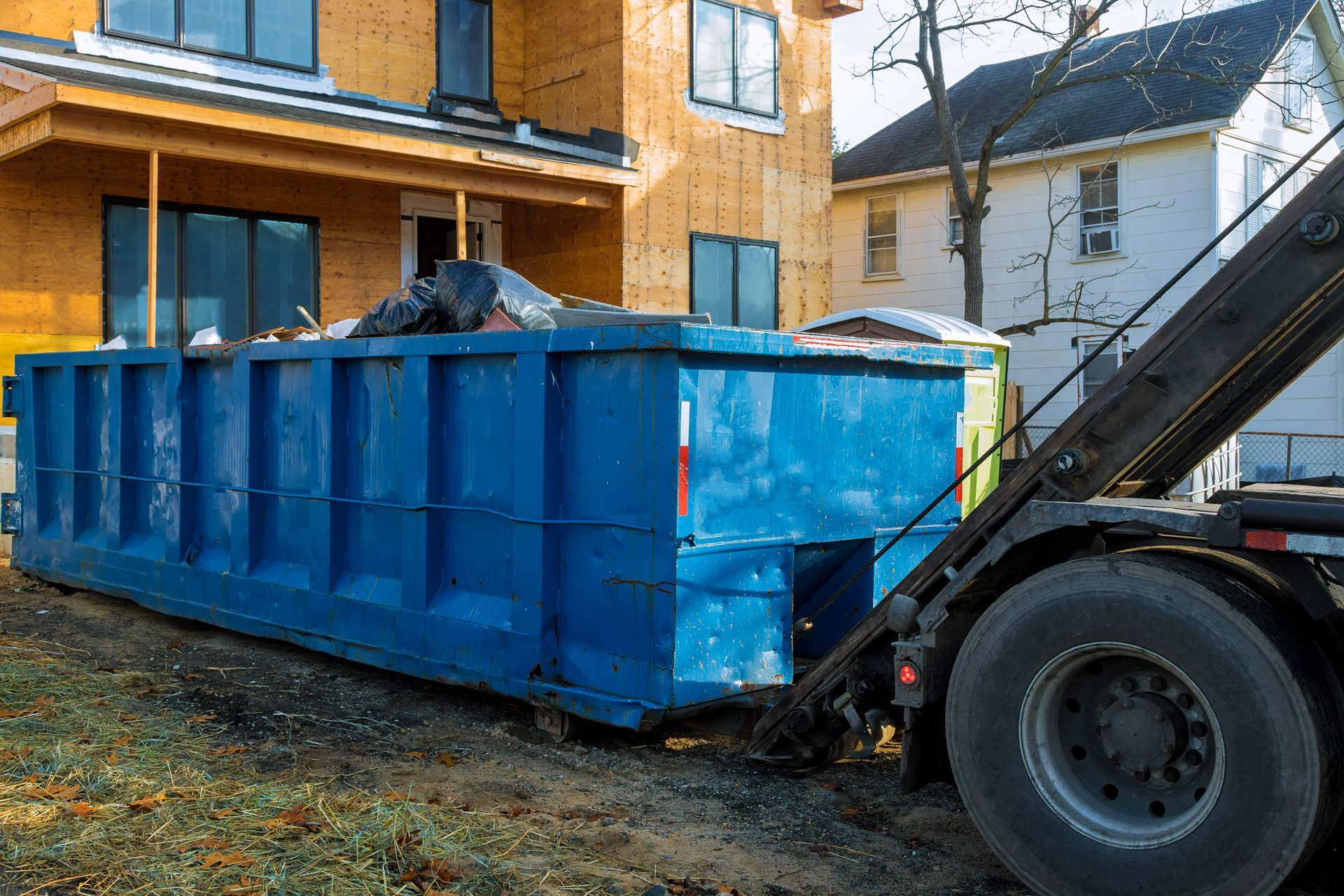 Blue dumpster filled with debris at a construction site, ready for pickup by a truck.