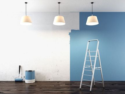 A room being painted; half white, half blue. Paint can, roller, ladder, and pendant lights.
