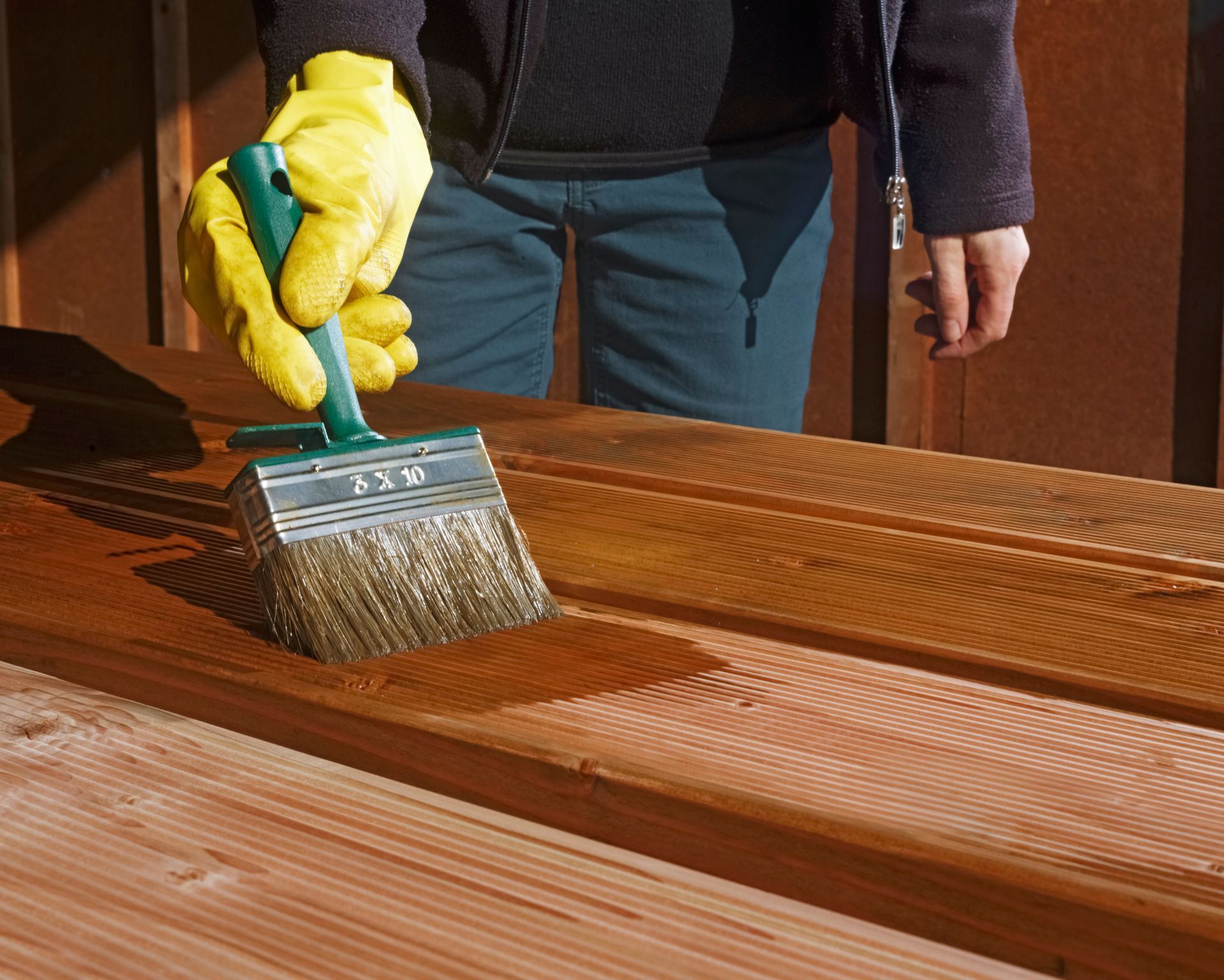 Person wearing gloves staining wooden planks with a brush.
