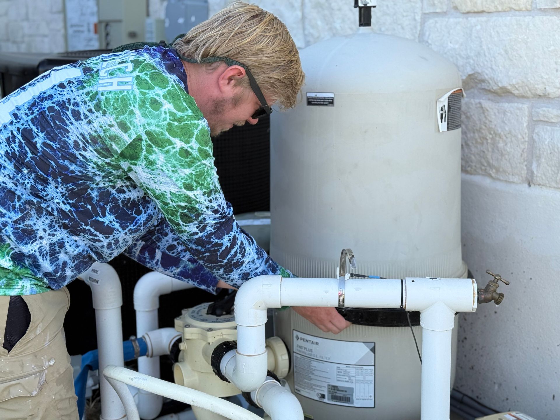 Man in tie-dye shirt inspecting a pool filter next to a wall.