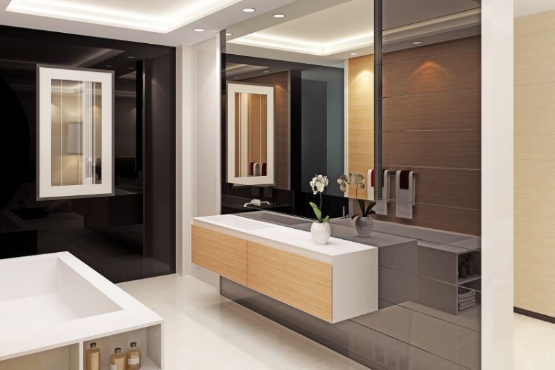 A white, free-standing bath, with toiletries sat on a small table next to it. There is a large mirror in the background, the floor is grey, as well as some of the walls, the rest of the walls are made out of oak and are bright.