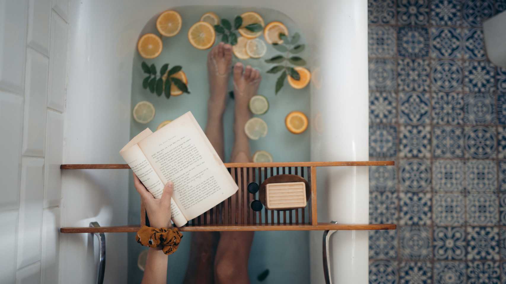 Bath with orange slices and leaves in the water. A book is in the image, held over a caddy bridge that has soap on it.