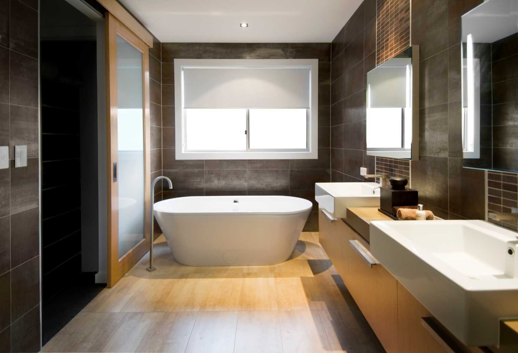 Bathroom with oak floor, modern black tiles on all walls, two sinks and two mirrors. The entrance is through a sliding door.