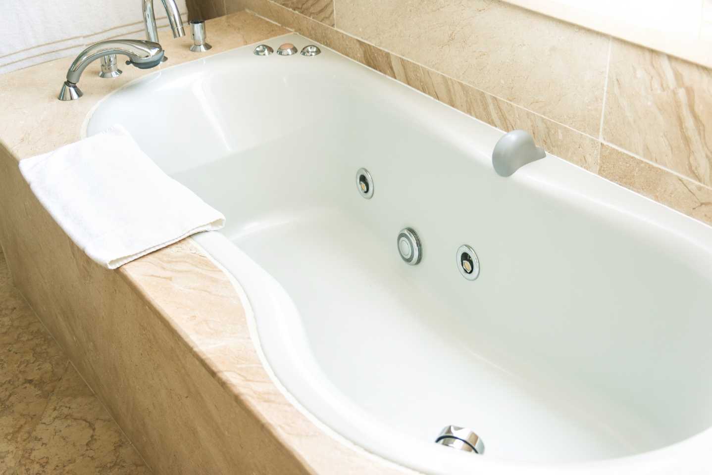 P-shape bath with no water in it. There is a towel on the side of the bath and jets in the bath.