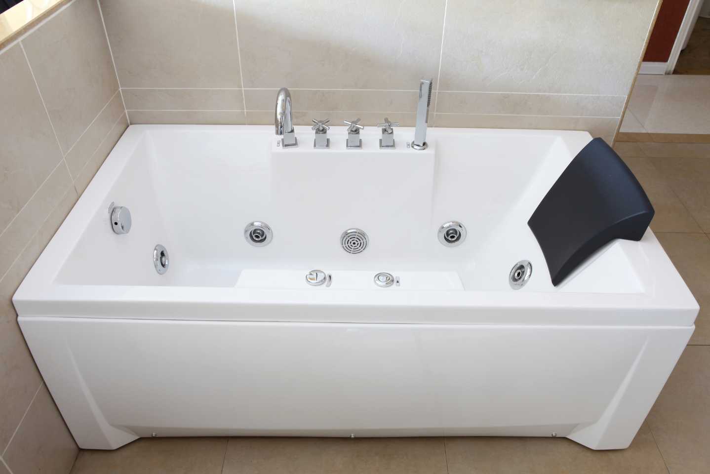 Whirlpool Bath with six jets in it, a back support at the right end, a tap and a shower head.