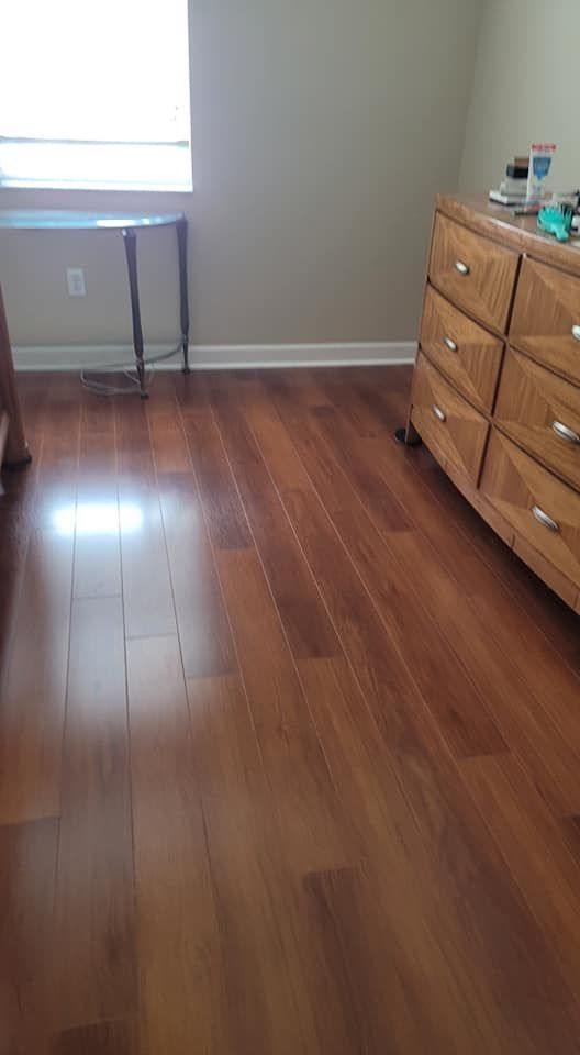 Hardwood floor in a room with a dresser and a small table near a window.