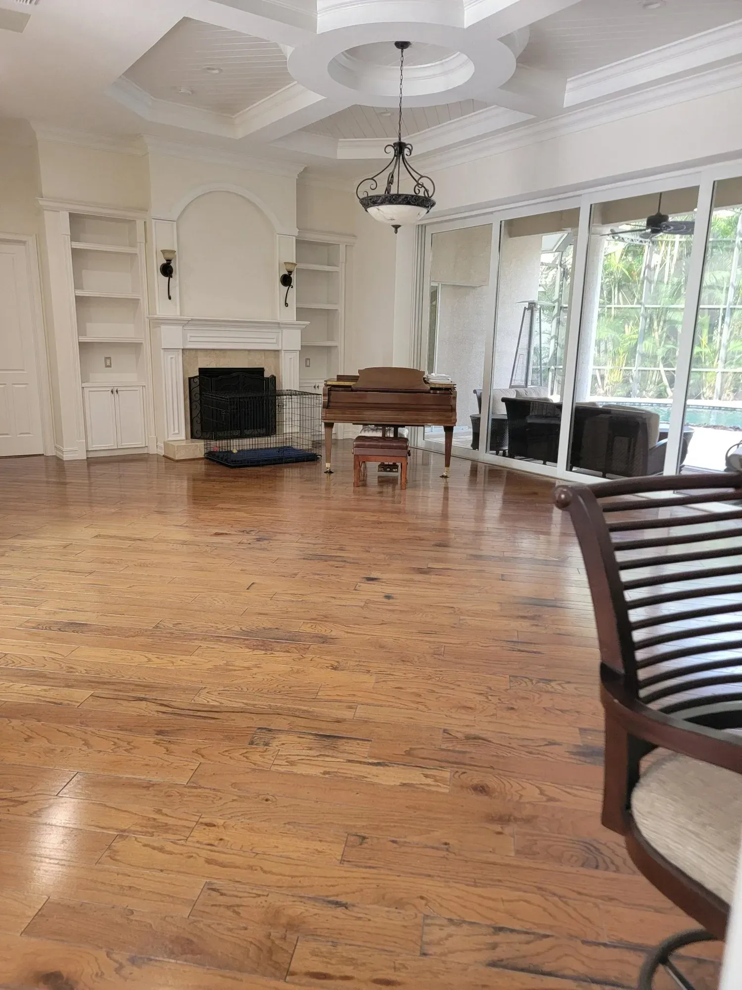 Large, empty living room with wood floors, fireplace, and a piano. Bright interior with tall windows.