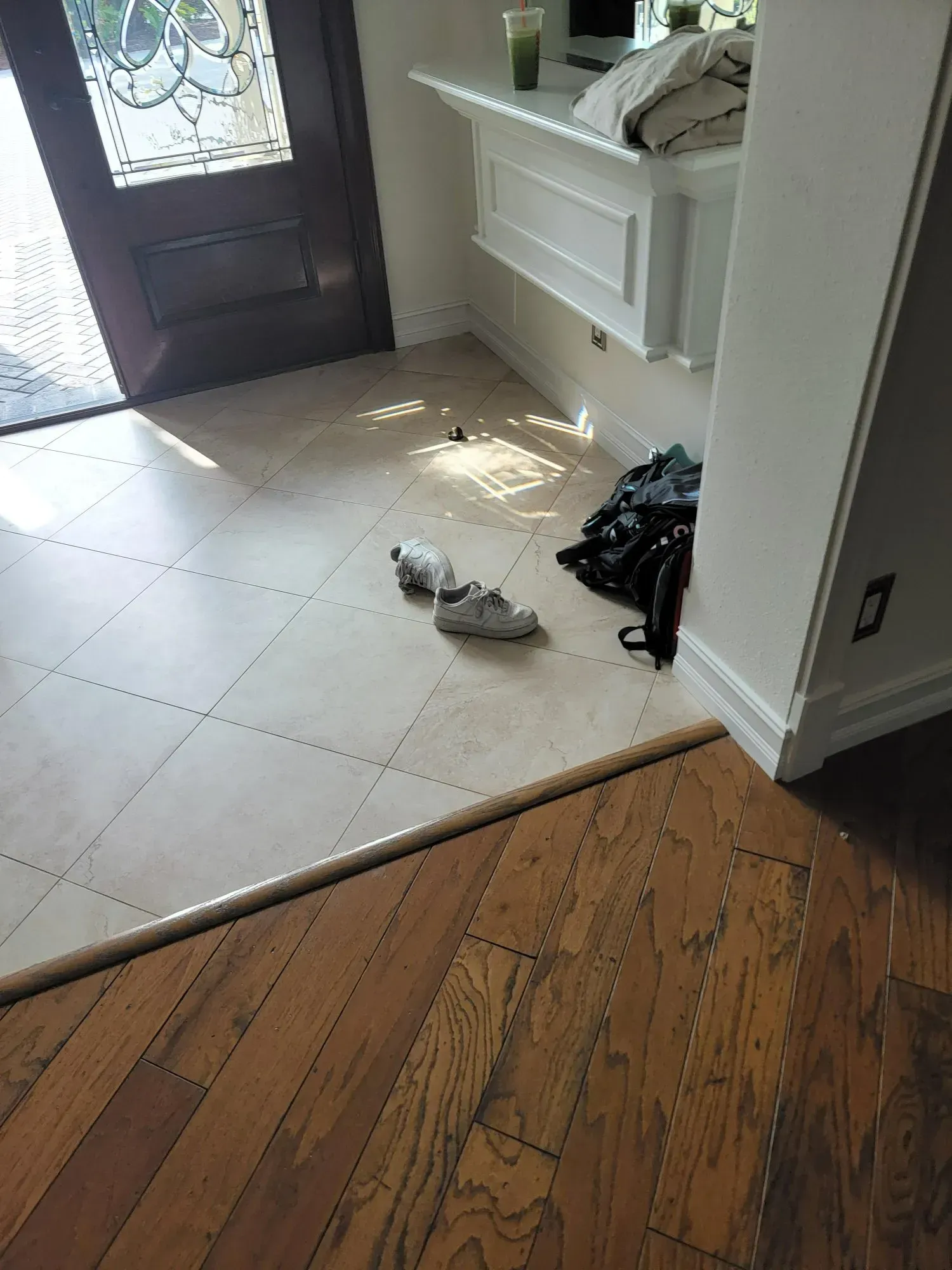 Entryway with wood and tile flooring, shoes, and a dark front door.