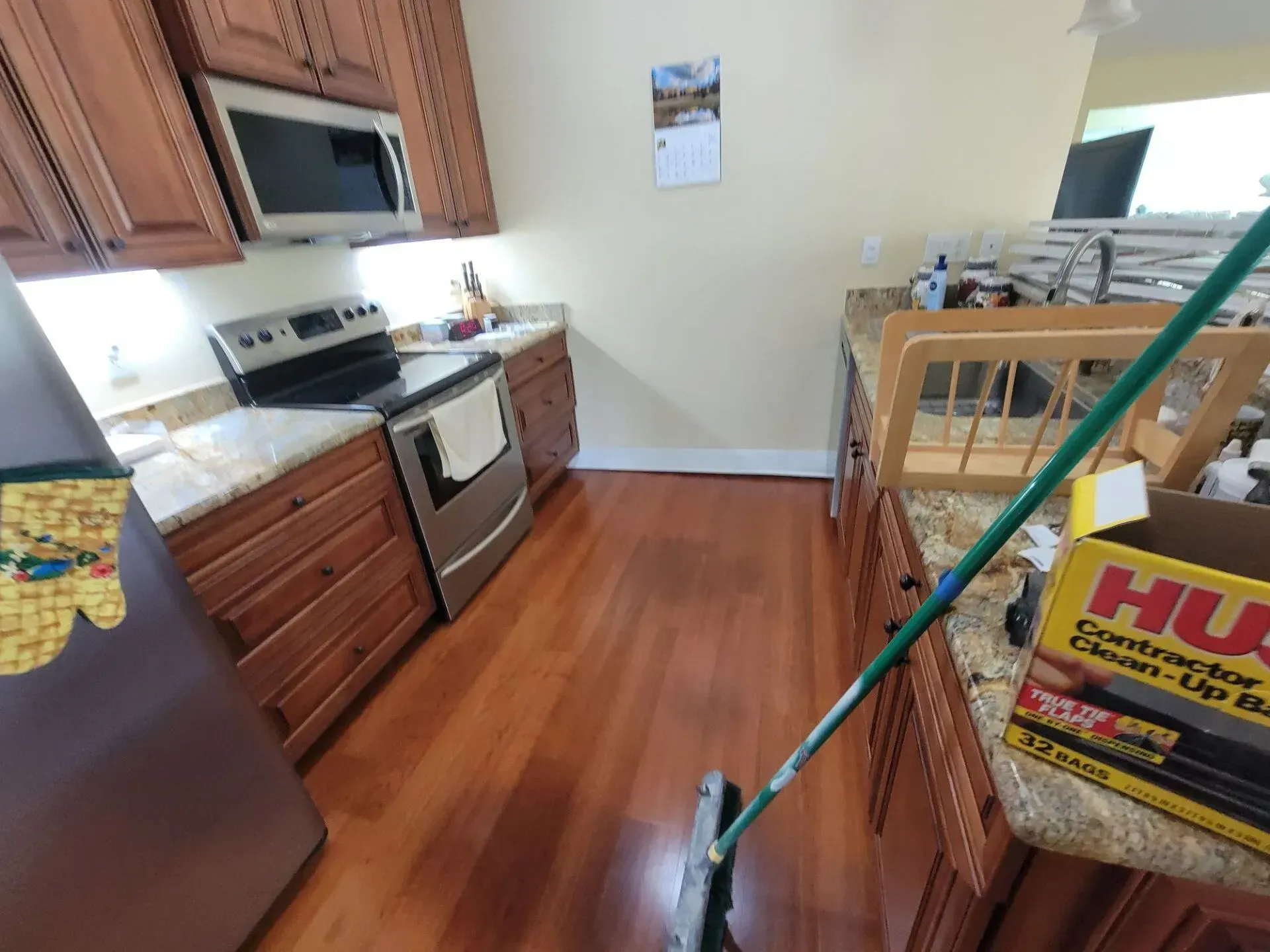 Kitchen with wooden cabinets, stainless steel appliances, and a mop in the foreground.