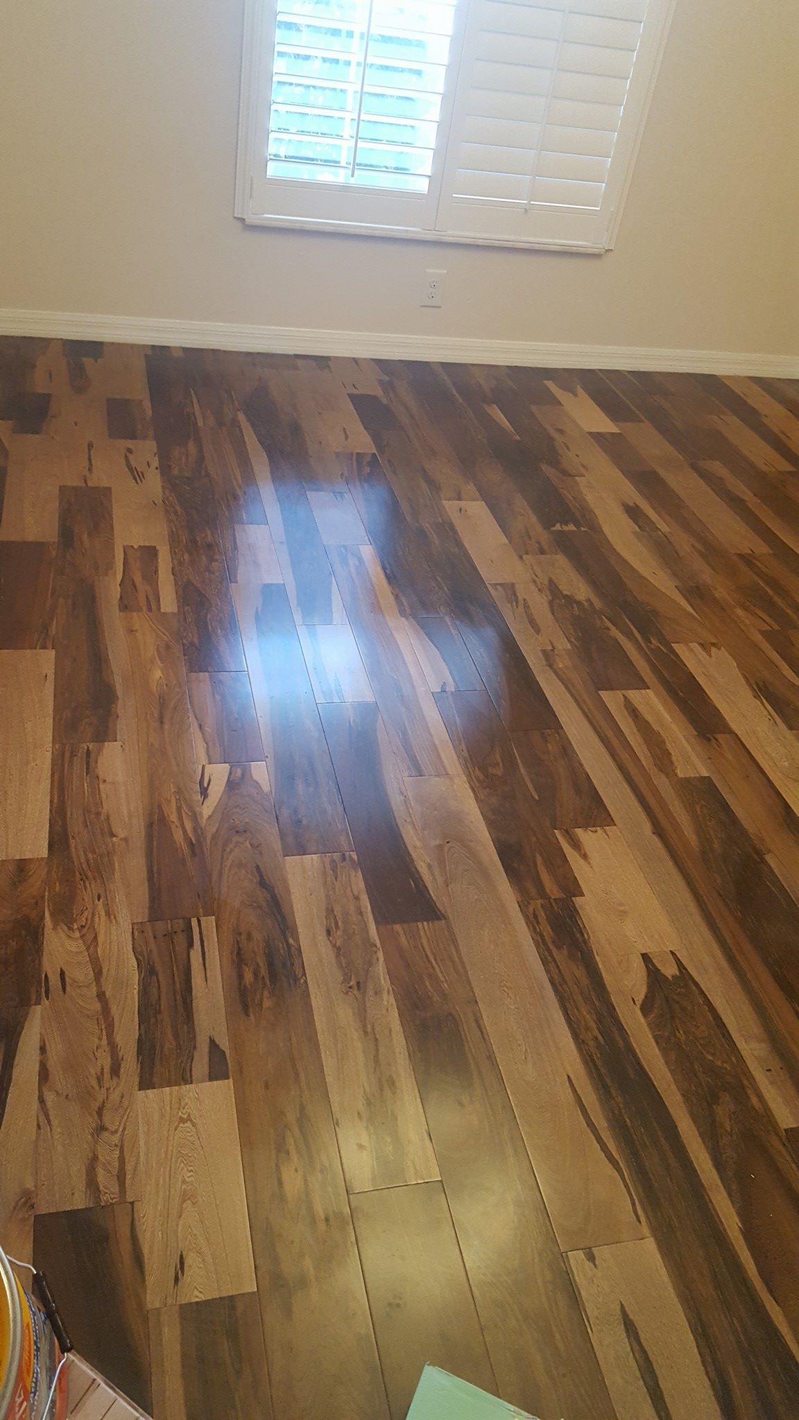 Wood-look laminate flooring in a room, with a window and white trim visible.