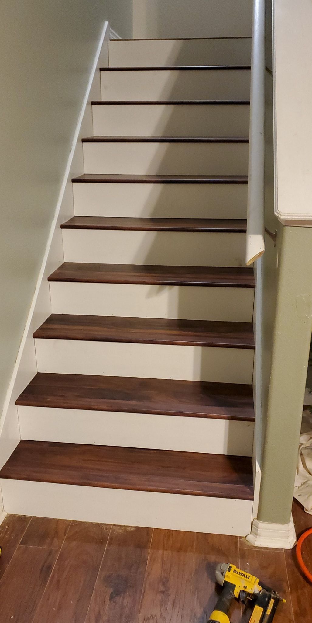 Staircase with stained wooden steps and white risers, leading upwards. A yellow drill rests on the floor.