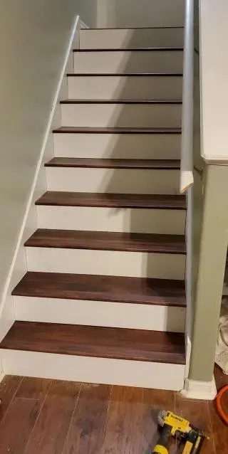Staircase with stained wooden steps and white risers, leading upwards. A yellow drill rests on the floor.