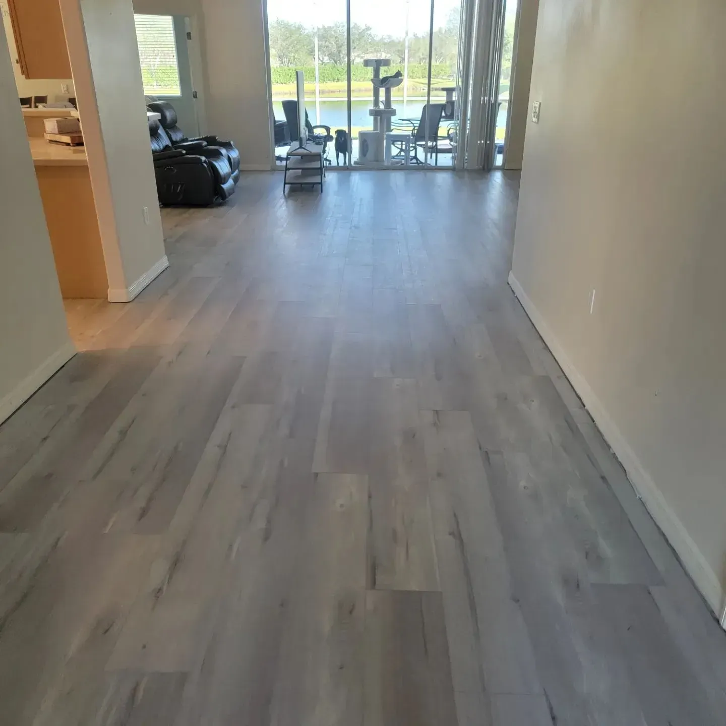 Gray wood-look flooring extends through an empty hallway toward a bright, sunny window overlooking a body of water.
