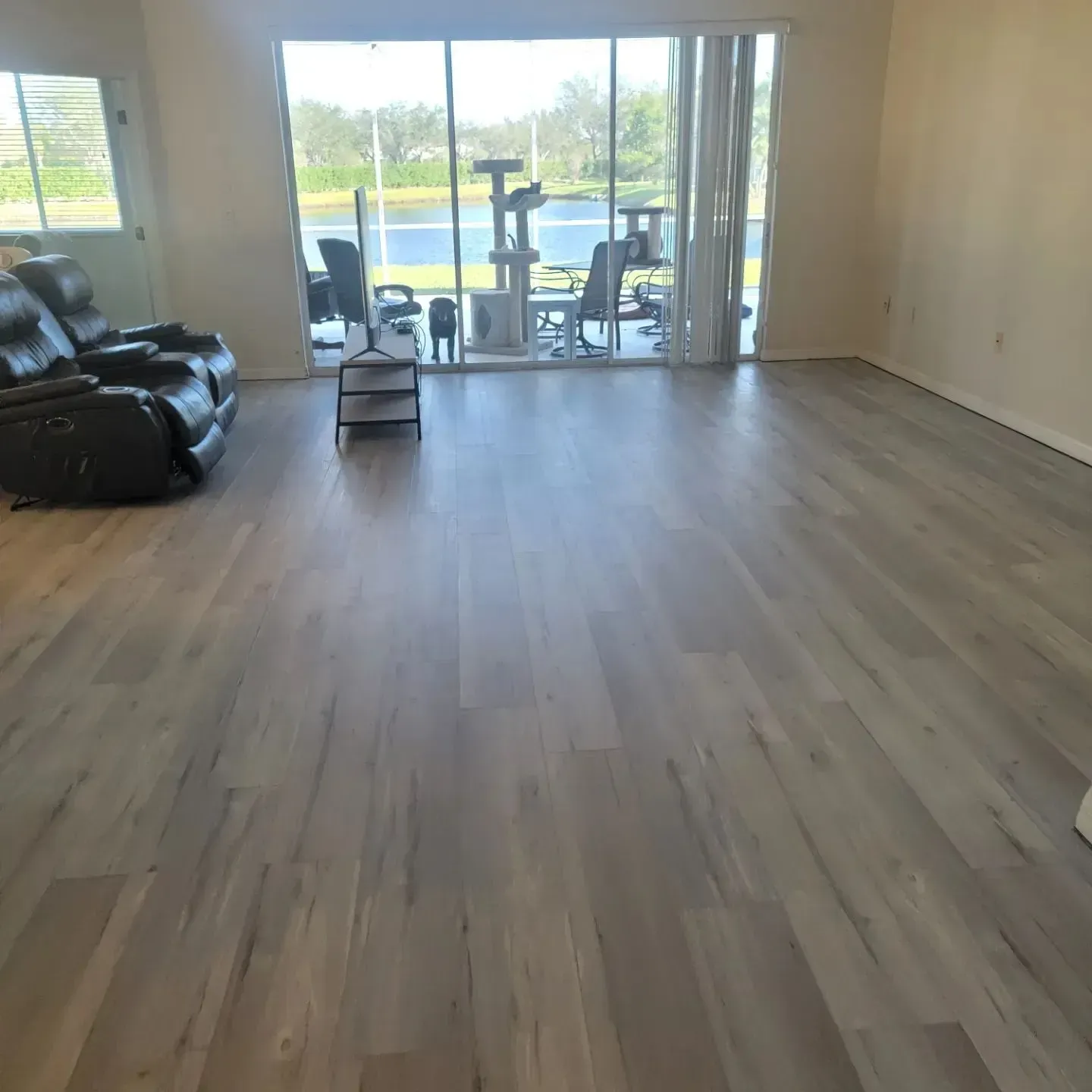 Light gray wood-look flooring in a living room, with a dark recliner, cat tree, and view of a lake.