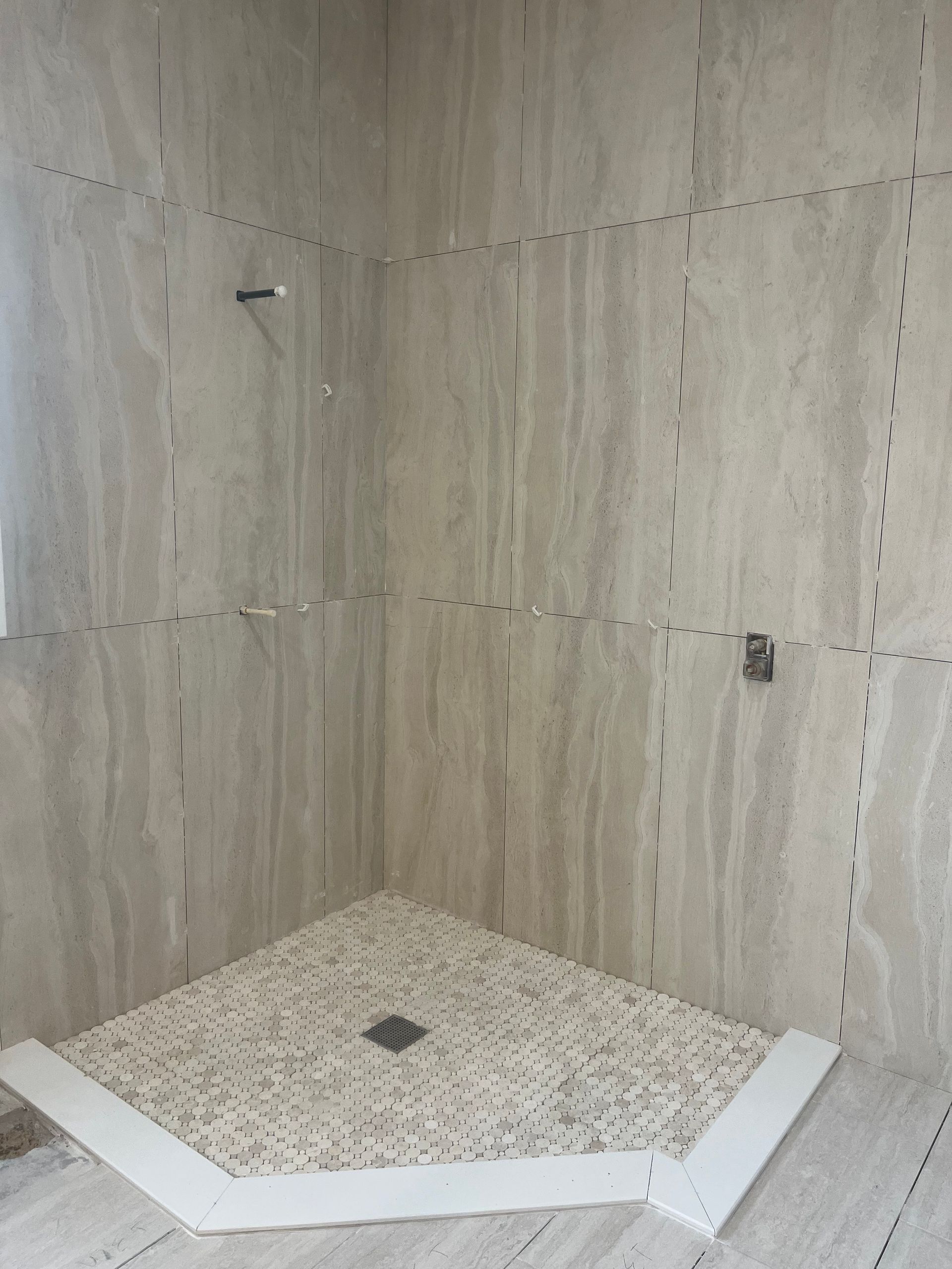 Empty tiled shower stall with a white hexagonal shower pan and a drain in the center.