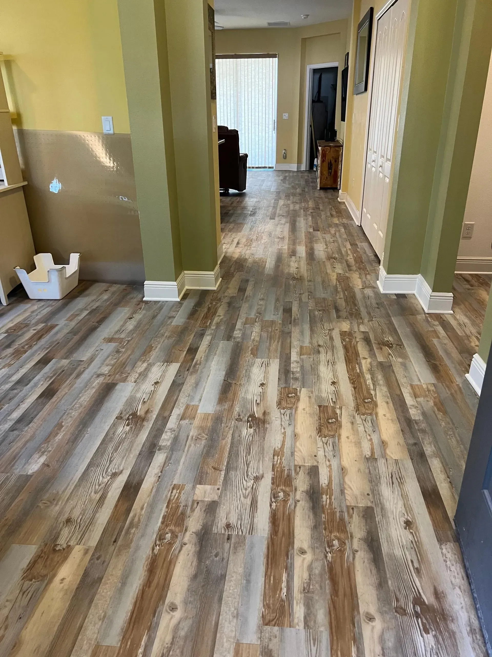 Hallway with weathered wood-look flooring and olive green pillars. Walls are tan and flooring has shades of brown and gray.