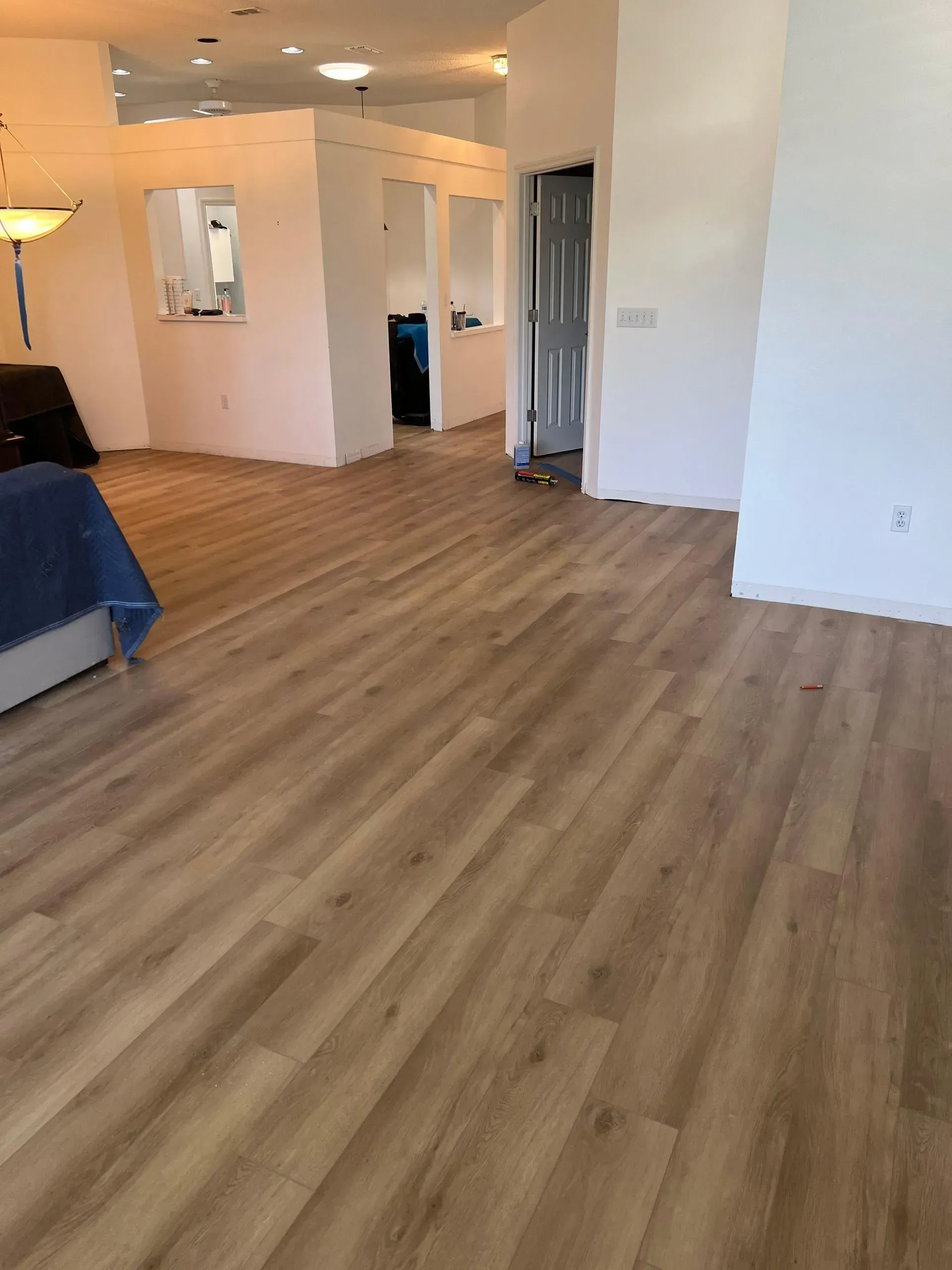 Light brown wood-look flooring extends throughout a spacious interior. White walls and partial dividers create open rooms.