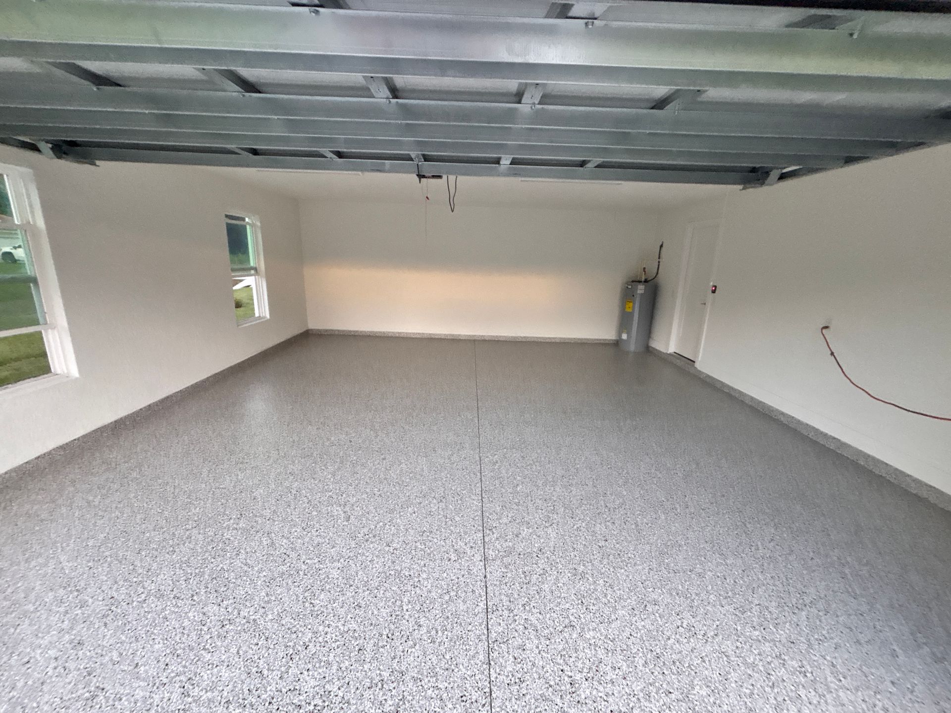 Empty unfinished garage with gray floor, exposed ceiling, windows, and a fire extinguisher on the right