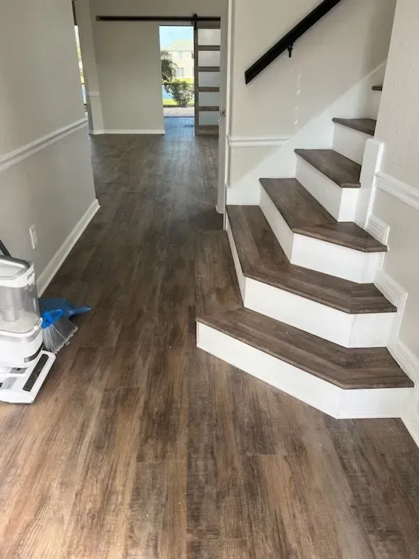 Interior view: Entryway with wood-look flooring, staircase with white risers, and a view of a hallway.
