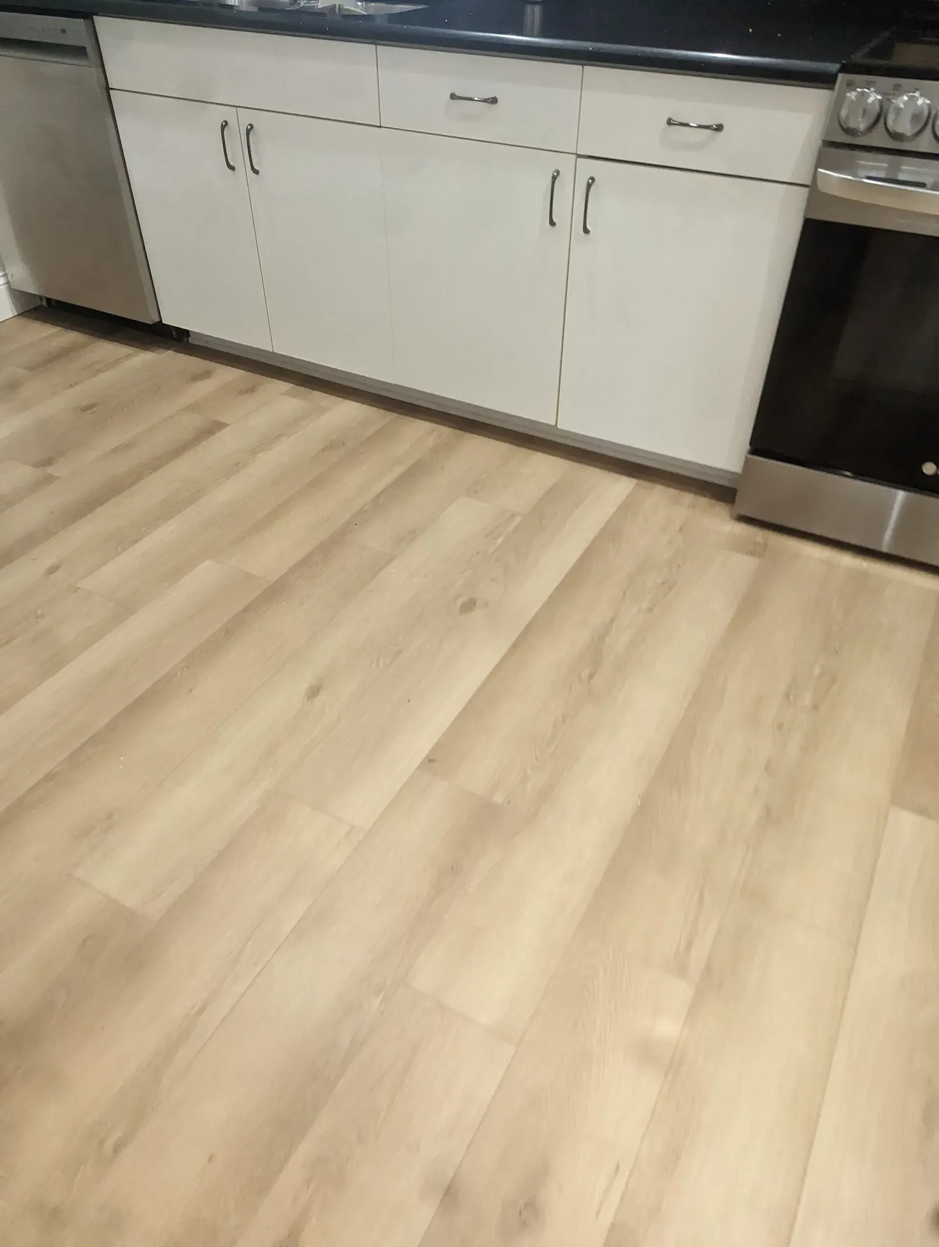 Light wood-look flooring in a kitchen with white cabinets, a black countertop, and a stainless steel oven.