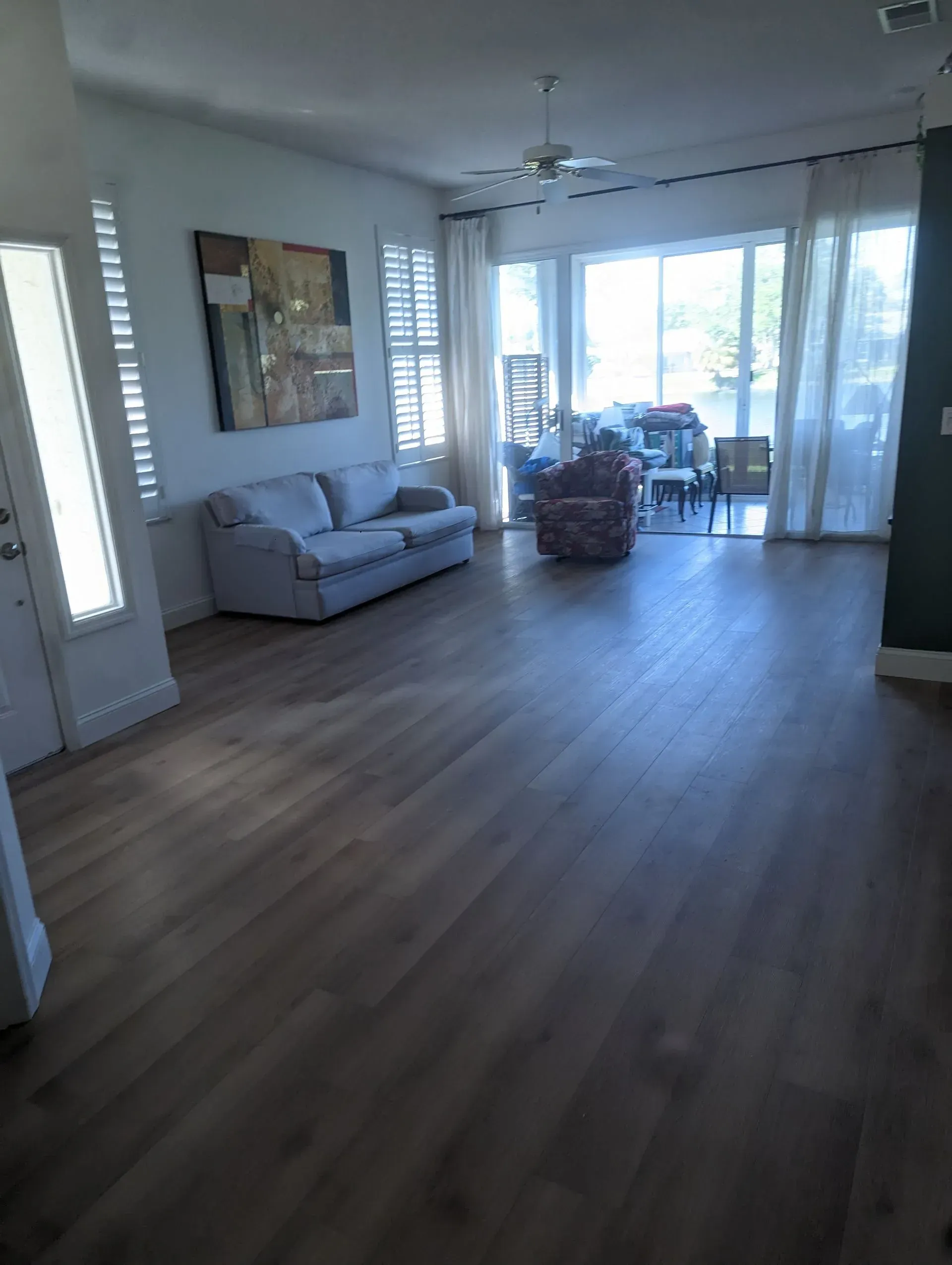 Living room with light wood floors, a blue sofa, and large windows with sheer curtains.