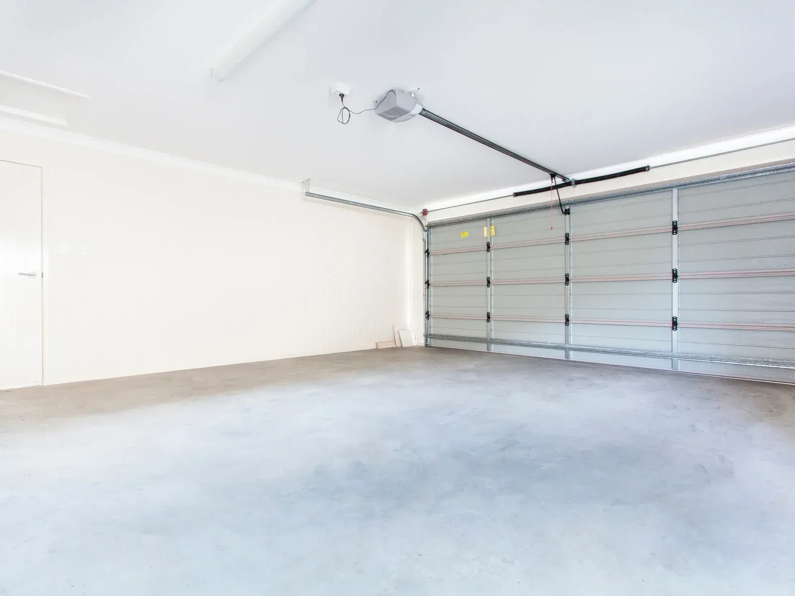 Empty garage with a closed, gray overhead door and concrete floor.