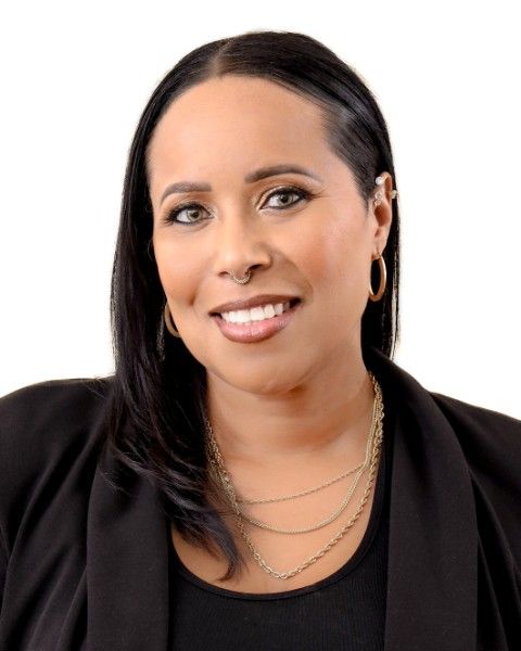 A woman wearing a yellow jacket and earrings is smiling for the camera.