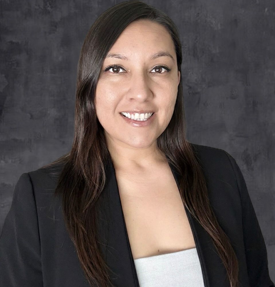 A woman wearing glasses and a grey jacket smiles for the camera