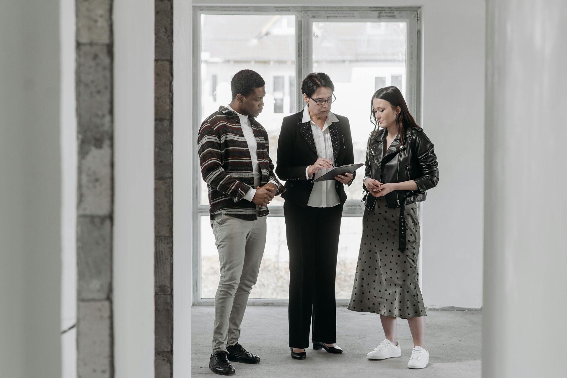 A group of people are standing in an empty room looking at a tablet.