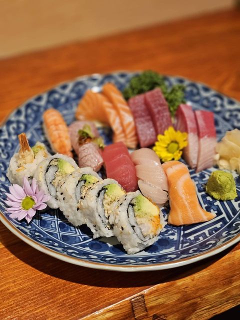 Assorted sushi and sashimi on a blue patterned plate with garnish on a wooden table