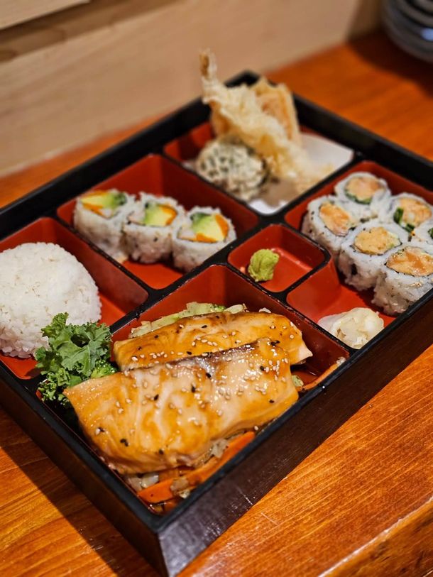 Sushi bento box with salmon, rolls, rice, and tempura on a wooden table